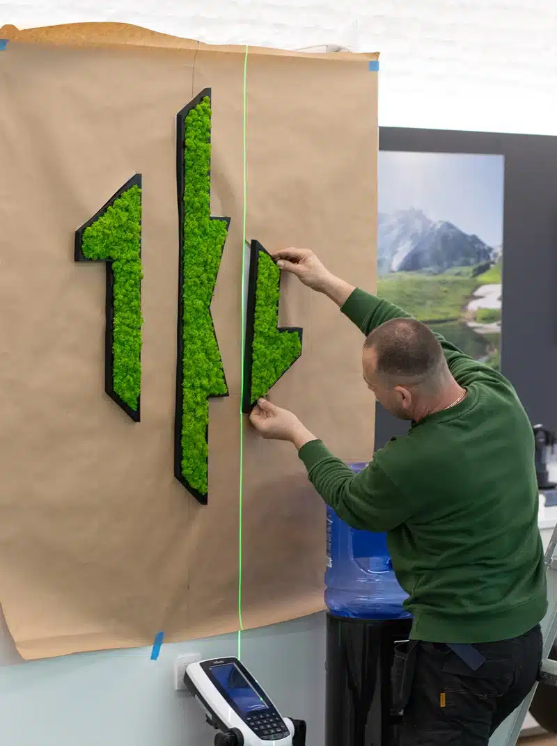Man adjusts green moss wall art pieces.